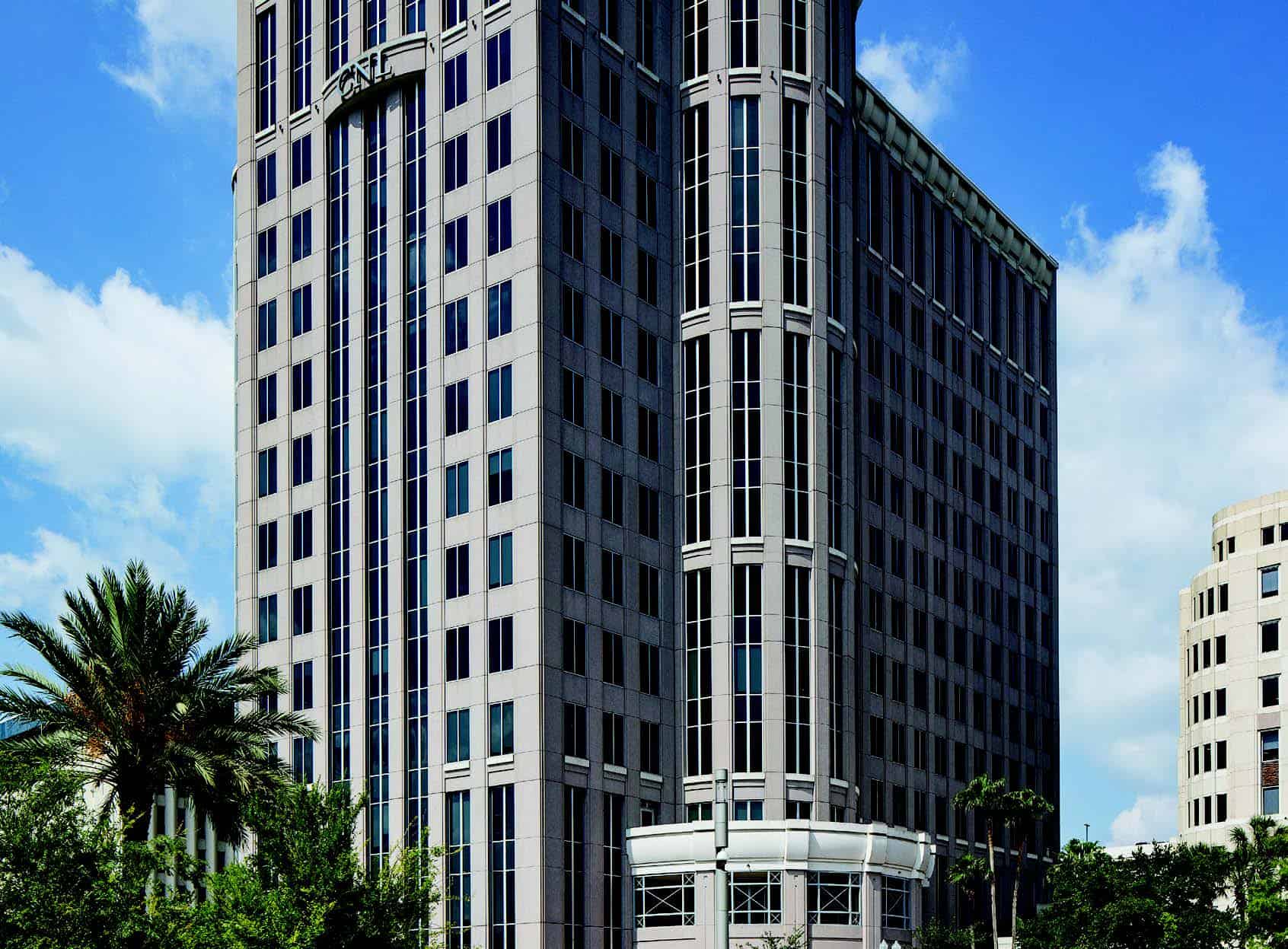 A tall, modern office building with many windows—home to Serendipity Labs coworking offices and meeting rooms—is surrounded by palm trees and greenery, standing against a blue sky dotted with scattered clouds.