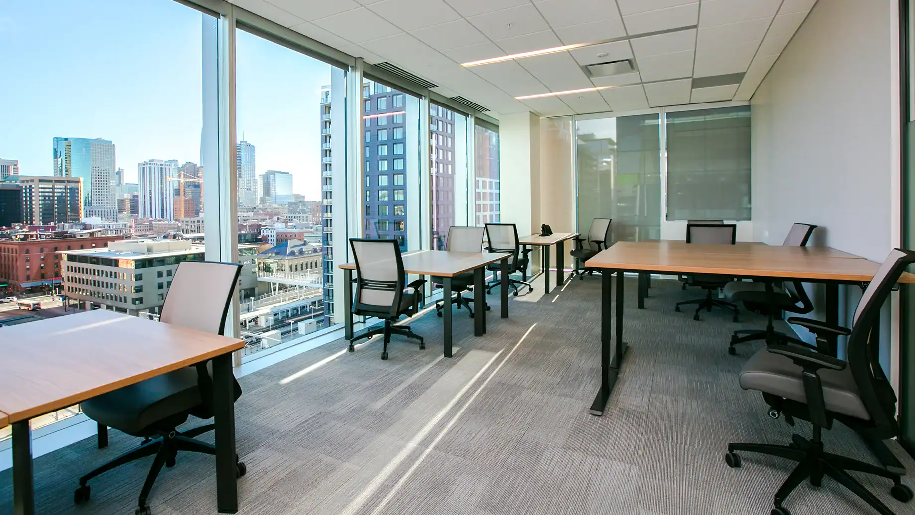 Modern office space with large windows overlooking a city skyline, featuring several desks and office chairs—Serendipity Labs coworking offers bright offices and meeting rooms filled with natural light throughout the workspace.